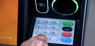 Close-up of an older hand entering a PIN on a metallic ATM keypad